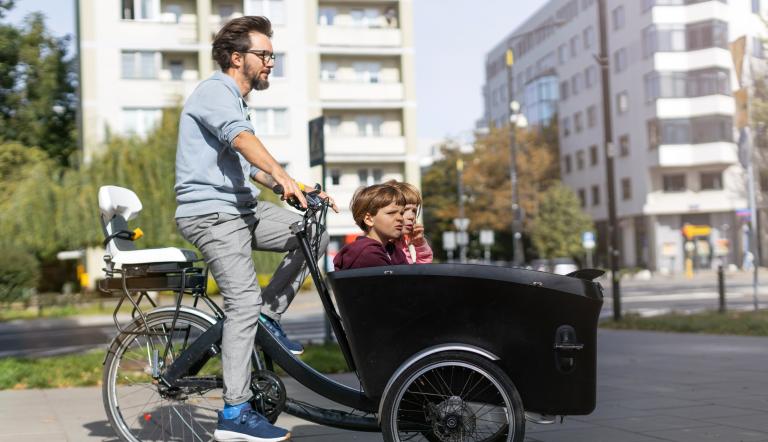 Ein Mann fährt auf einem Lastenrad mit Kindern vorne im Kasten.