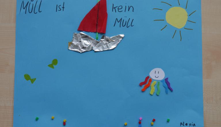 Auf blauem Papier befindet sich ein Schiff und eine Krake, die aus recycelten Material aufgeklebt wurden.