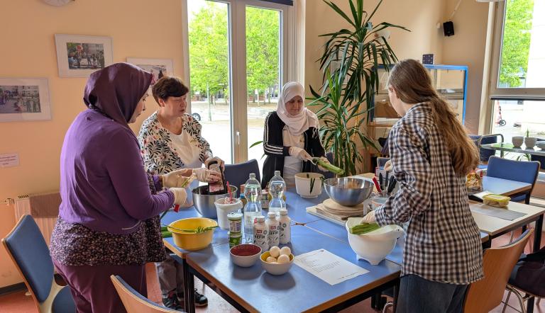 Vier Frauen bereiten an einem Tisch ein Gericht zu.