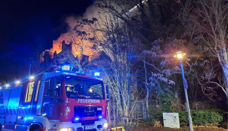 Ein Feuerwehrauto steht vor der brennenden Villa.