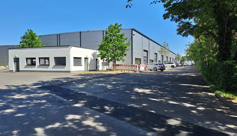 Industriehalle mit kleinem Verwaltungsgebäude im Vordergrund, auf der rechten Seite befinden sich Parkplätze