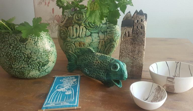 Auf einem Tisch stehen mehrere Keramikwerke zusammen, darunter weiße Schalen, grüne Blumentöpfe, ein brauner turm und ein grüner Fisch.