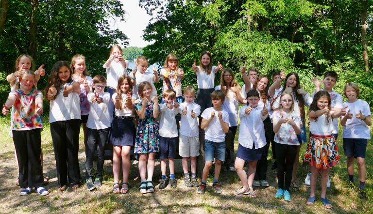 La Corista - Thumbs Up! Eine große Kinderschar steht in der Natur und streckt Hände vor und Daumen nach oben. Der Kinderchor La Corista hat ein Konzert.