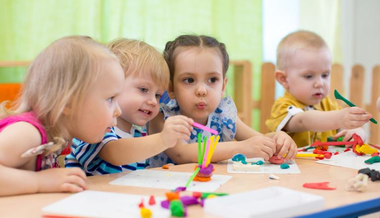 Vier Kita-Kinder sitzen an einem Tisch und basteln mit bunter Knete.