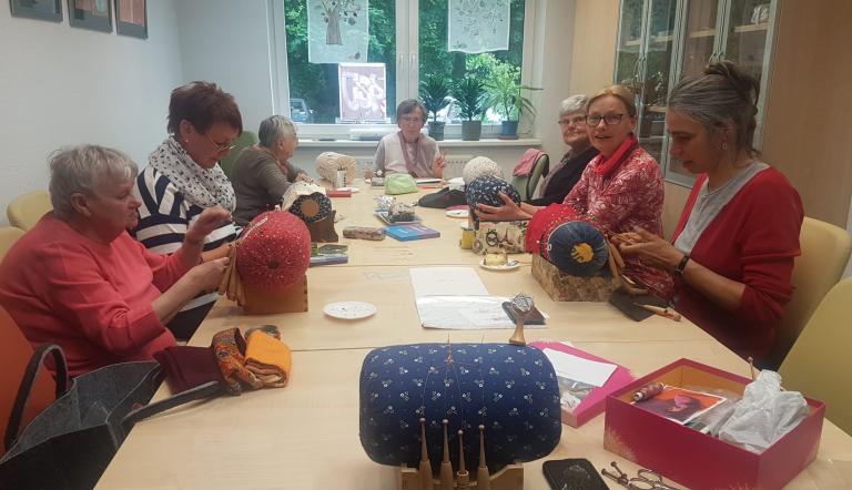 Sieben Frauen sitzen an einem Tisch und arbeiten jeweils an einer Klöppelstation.
