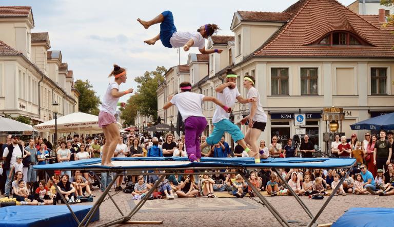Menschen springen auf einem Trampolin in der Innenstadt, darum sammelt sich eine Gruppe Zuschauende