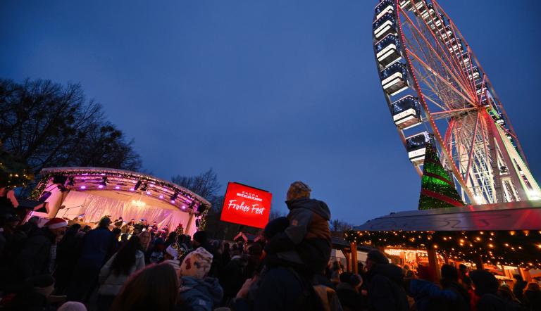 Unter blauem Nachthimmel sehen wir das beleuchtete Riesenrat und viele Menschen, die zu einer schönen Bühne strömen