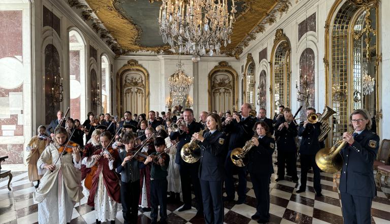 Im prächtigen Saal von Schloss Sanssouci musizieren viele uniformierte Berufsmusiker*innen und Kinder in historischen Gewändern