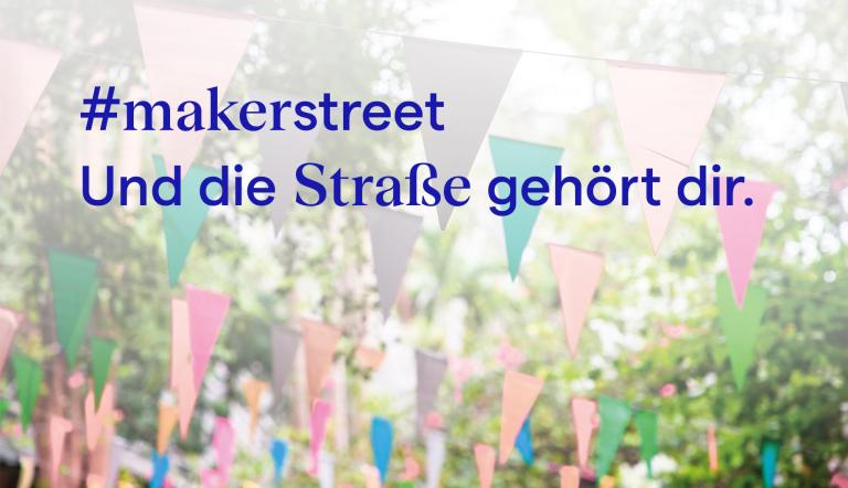 Schrift über Wimpeln, die in den Bäumen gespannt sind.