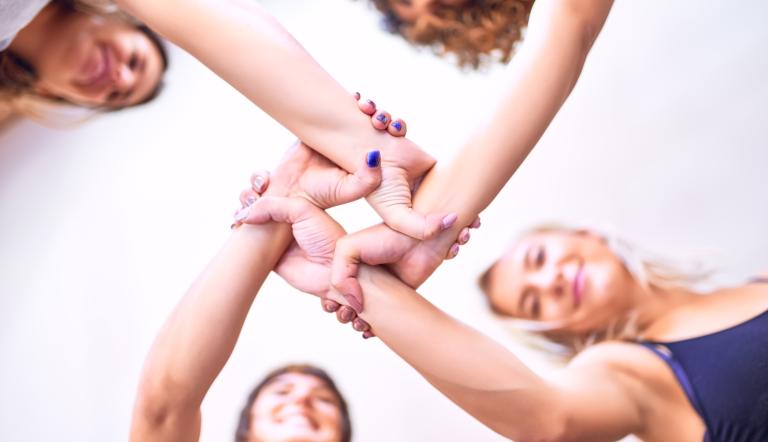 Vier Frauen halten sich an den Handgelenken und bilden damit einen Kreis.