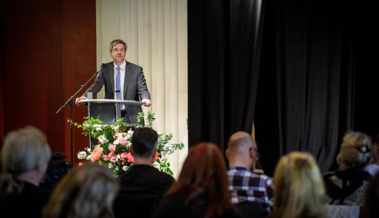 Oberbürgemeister Mire Schuber steht am Rednerpult, unten im Bild sieht man Köpfe vom Publikum