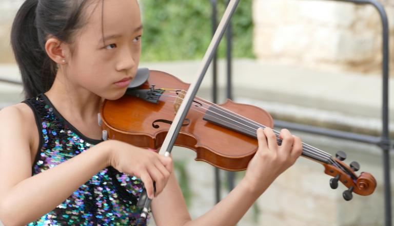 Junge Violinistin spielt ihr Instrument im Freien, unscharfer schöner Hintergrund
