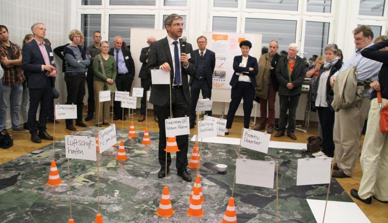Der Obermeister Mike Schubert erläutert mit Fähnchen die wichtigsten Projekte der Zukunft auf einem Stadtteppich (Foto: Landeshauptstadt Potsdam / Barbara Plate)