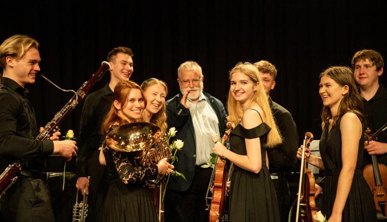 Gäste des JSO aus der Partnerstadt Opole (@Uwe Hauth) Einige junge klassische Musikerinnen und Musiker freuen sich über einen gelungenen Auftritt und posieren mit ihren Instrumenten. In ihrer Mitte der Leiter der Gruppe aus Opole namens Hubert Prochota. Er ist weißhaarig und hat einen weissen Bart. Auch er freut sich sichtlich!