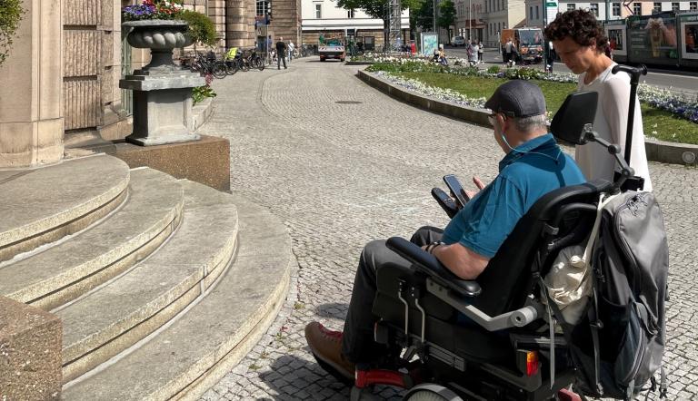 Das Foto zeigt einen Rollstuhlfahrer mit der Beauftragten für Menschen mit Behinderung, Dr. Tina Denninger