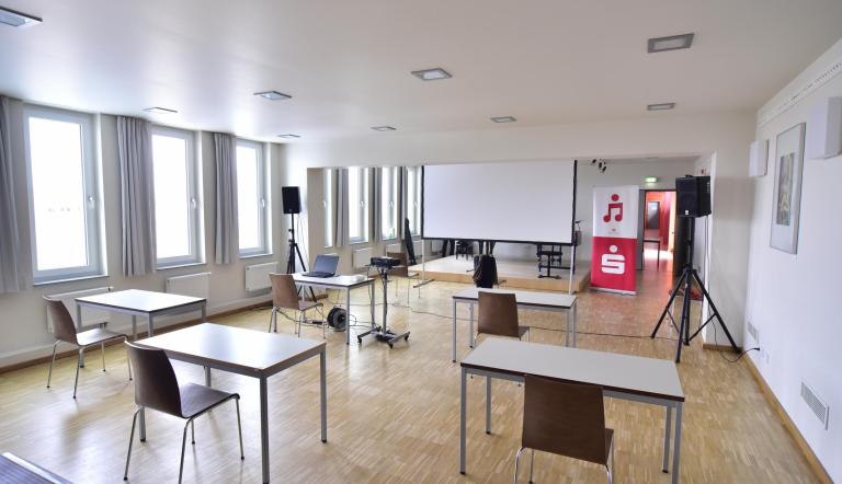 Jugend Musiziert Wettbewerb Hybrid 2021 Tische, Stühle und eine BEamerleinwand sind für eine Hybridveranstaltung des Wettbewerbes Jugend Musiziert in einem Raum der Musikschule am Campus am Stern aufgebaut.