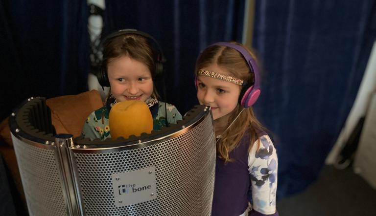 Kinderchorsängerinnen im Studio Zwei kleine Mädchen froh lächelnd in einer kleinen mobilen Aufnahmekabine mit Mikrophonen