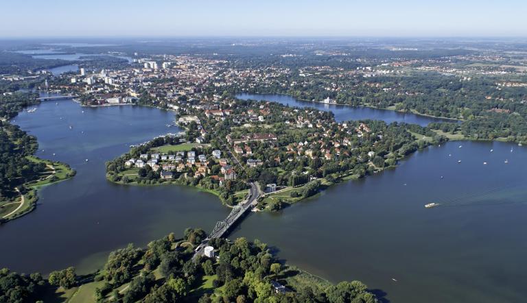 Das Bild zeigt Potsdam aus der Vogelperspektive - vorn die Glienicker Brücke, dahinter die Berliner Vorstadt, umrahmt von der Seenlandschaft und den UNESCO-Welterbeparks.