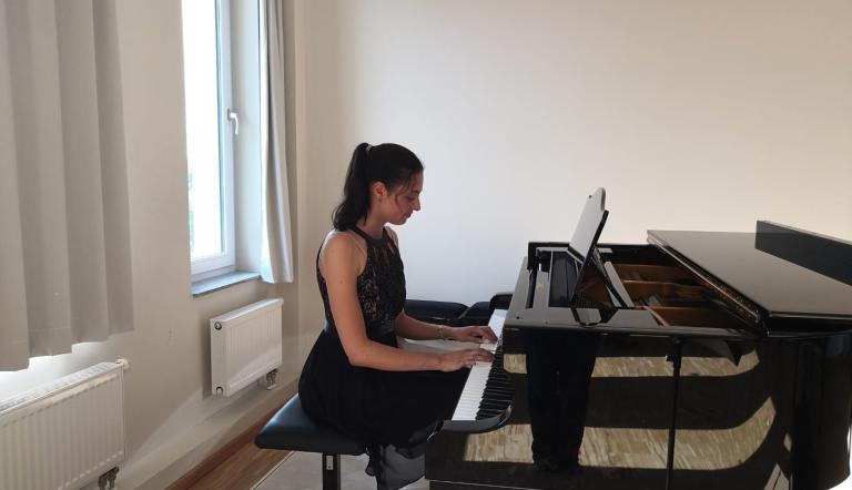 Hier erscheint ein Bild mit einer Bühne im Kammermusiksaal der städtischen Musikschule. Eine Pianistin spielt auf einem Konzertflügel
