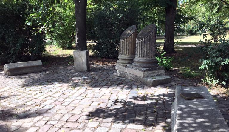 Das Foto zeigt Säulen-Fragmente des ehemaligen Stadtschlosses mit den Portraits von Voltaire und Lessing auf Bronzeplatten. Rechts davon ein Buch aus Bronze, links ein bronzenes Tintenfass mit Feder - jeweils auf Stein-Fragmenten des ehemaligen Stadtschlosses.