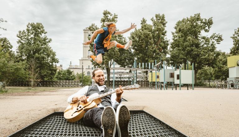 Mann mit Gitarre auf einem Trampolin, dahinter springt ein Mensch, Foto: der bunte hund, Lizenz: der bunte hund