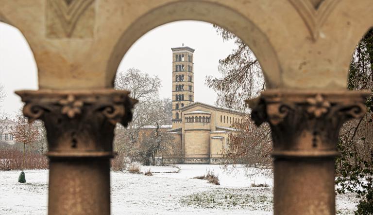 Verschneiter Park mit Kirchturm im Hintergrund, gesehen durch leicht unscharfe steinerne Bögen und Säulen im Vordergrund., Foto: André Stiebitz, Lizenz: PMSG