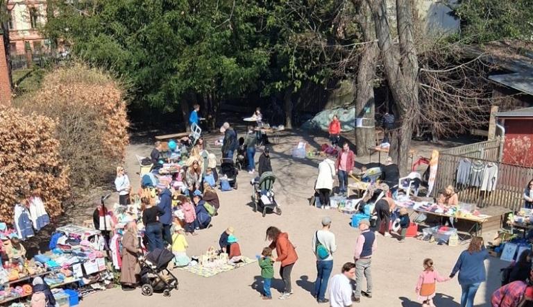 Flohmarkt im Freien mit Ständen für Kleidung und Spielzeug, viele Erwachsene und Kinder auf einem Platz unter Bäumen., Foto: Förderverein Erlöserkita, Lizenz: Förderverein Erlöserkita