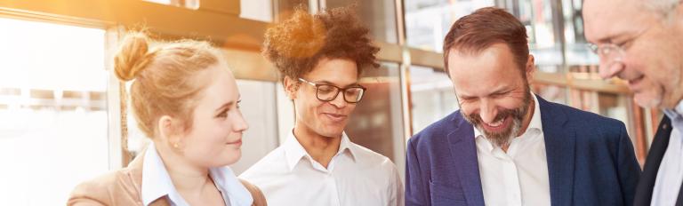 4 Personen im Büro, die freundlich lächeln und auf einem Blatt Papier schauen