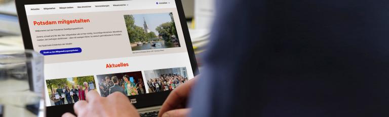 Zu sehen ist ein Notebook mit der Startseite von mitgestalten.potsdam.de, vor dem eine Person sitzt und auf der Tastatur tippt.
