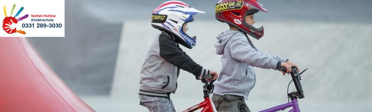 Vorschulkinder fahren Fahrrad, die Notfall-Hotline Kinderschutz von Potsdam ist zu sehen: 0331 289 3030