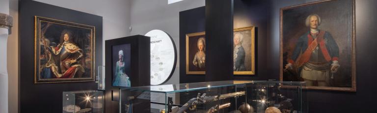 Das Foto zeigt einen Raum der Brandenburg - Ausstellung im Haus der Brandenburgisch-Preußischen Geschichte. Zu sehen sind Gemälde und Vitrinen mit Ausstellungsstücken. (© BKG,