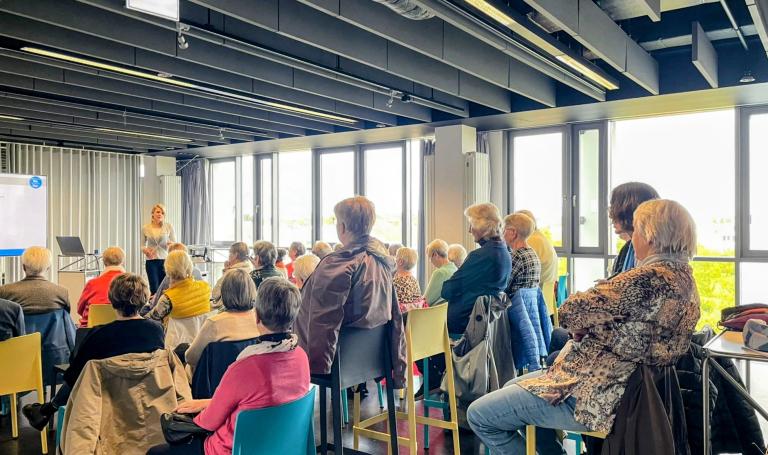 Mehrere Menschen nehmen an einem Vortrag teil und schauen nach vorn.