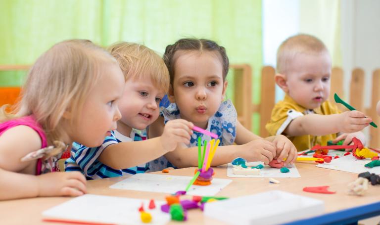 Vier Kita-Kinder sitzen an einem Tisch und basteln mit bunter Knete.