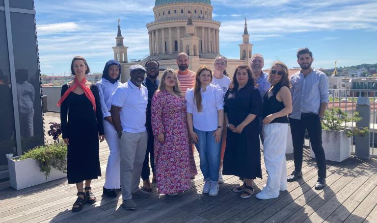 Auf dem Foto sind Frauen und Männer des Migrantenbeirates zu sehen. Sie stehen auf der Terasse des Bildungsforums, im Hintergrund ist die Nikolaikirche zu sehen.